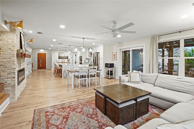 living room featuring a brick fireplace, light hardwood / wood-style floors, and ceiling fan