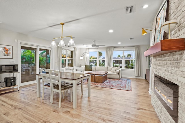 dining area featuring ceiling fan, a brick fireplace, and light hardwood / wood-style floors