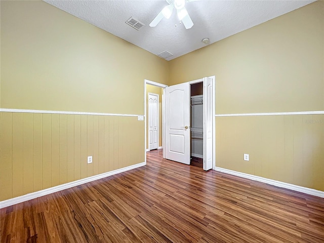 unfurnished bedroom with hardwood / wood-style floors, wood walls, ceiling fan, a textured ceiling, and a closet