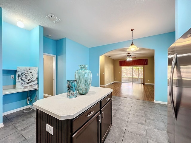 kitchen with a center island, stainless steel refrigerator with ice dispenser, decorative light fixtures, ceiling fan, and dark brown cabinets