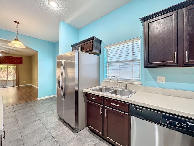 kitchen with appliances with stainless steel finishes, dark brown cabinets, a textured ceiling, sink, and hanging light fixtures