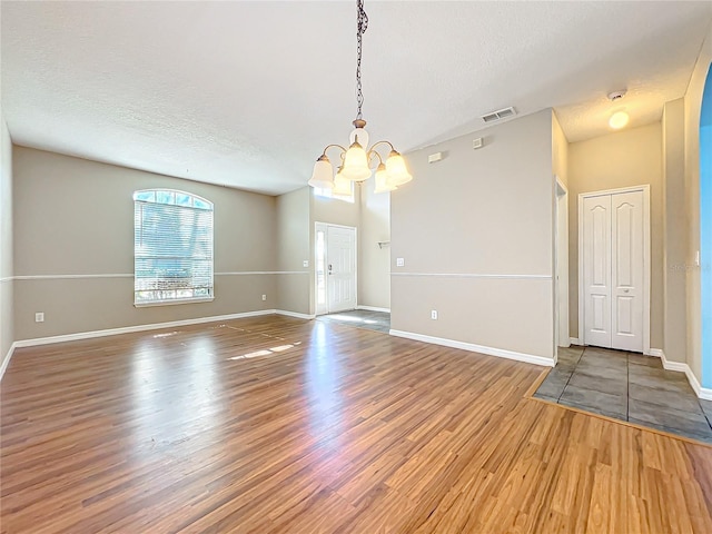 spare room featuring a chandelier, hardwood / wood-style floors, and a textured ceiling