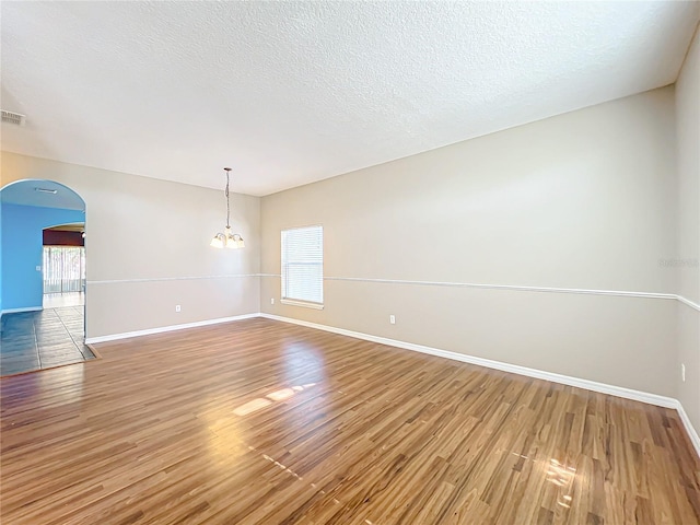 unfurnished room featuring a textured ceiling, a notable chandelier, and hardwood / wood-style flooring