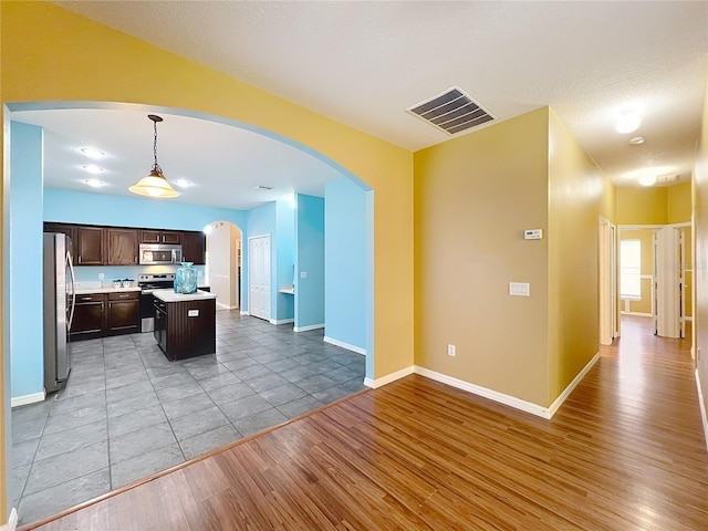 kitchen featuring dark brown cabinets, stainless steel appliances, decorative light fixtures, light hardwood / wood-style floors, and a kitchen island