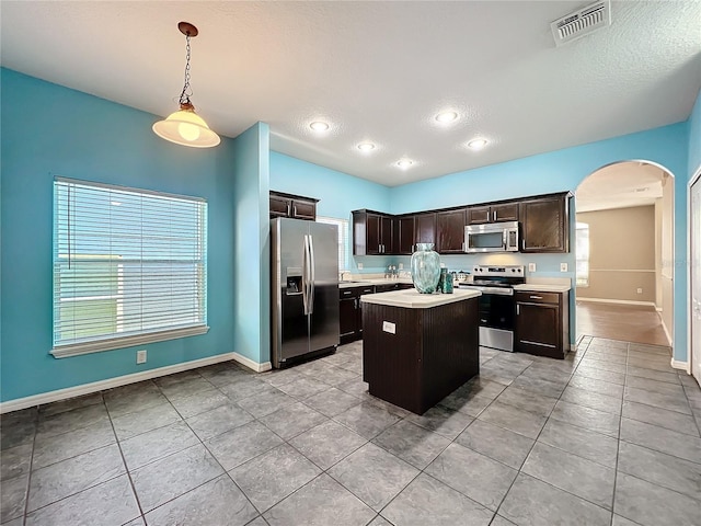 kitchen with a center island, stainless steel appliances, decorative light fixtures, dark brown cabinets, and light tile patterned floors