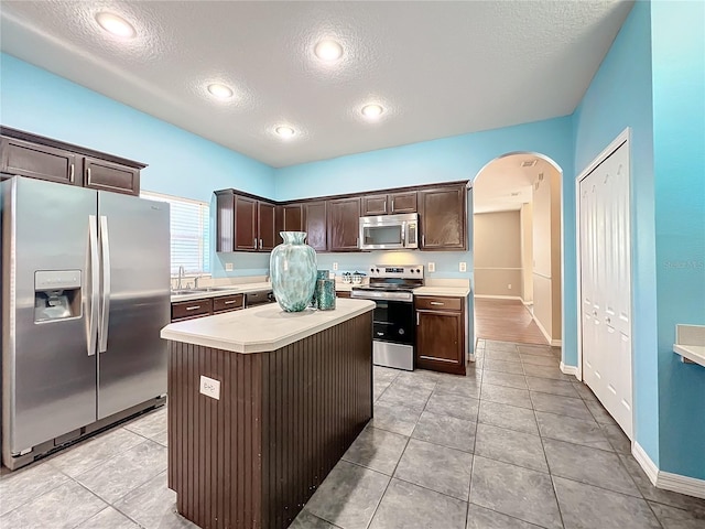 kitchen featuring dark brown cabinets, a textured ceiling, stainless steel appliances, a center island, and light tile patterned flooring