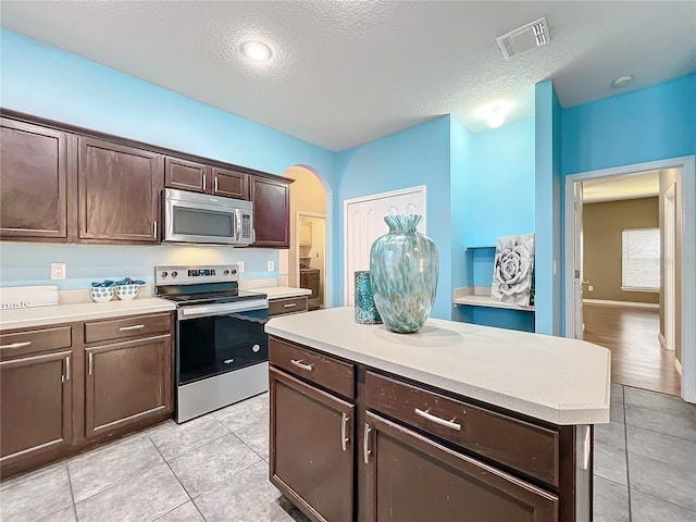 kitchen featuring appliances with stainless steel finishes, a textured ceiling, a kitchen island, and dark brown cabinets