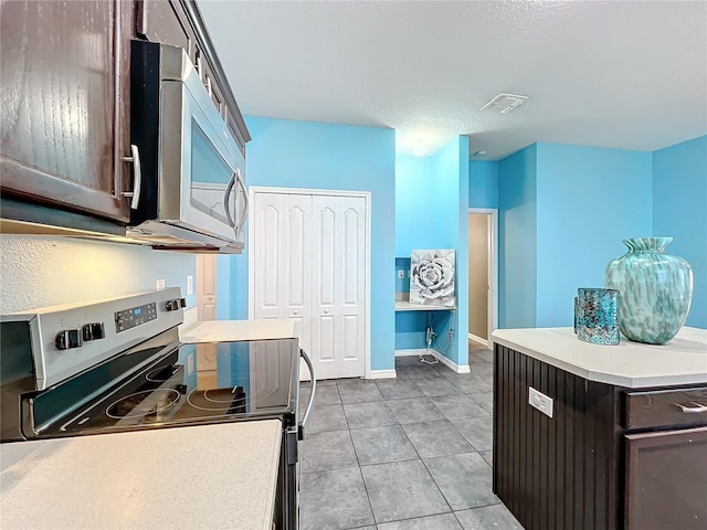 kitchen with appliances with stainless steel finishes, a textured ceiling, light tile patterned floors, and dark brown cabinets