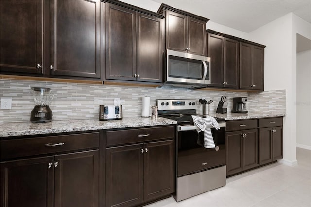 kitchen featuring light stone countertops, decorative backsplash, dark brown cabinets, light tile patterned floors, and appliances with stainless steel finishes