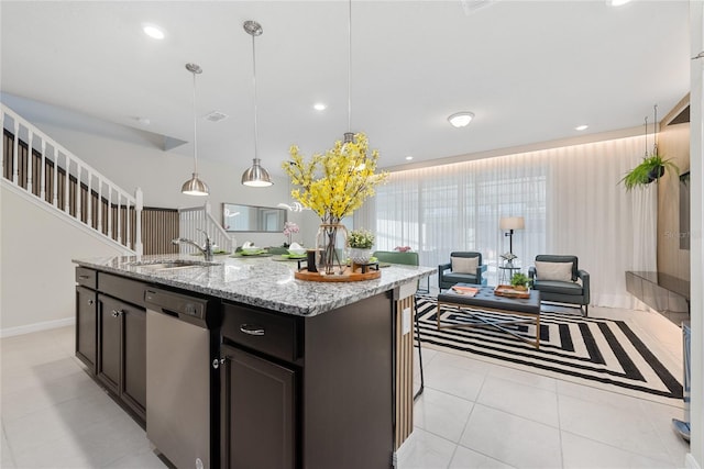 kitchen featuring light stone countertops, stainless steel dishwasher, sink, pendant lighting, and an island with sink