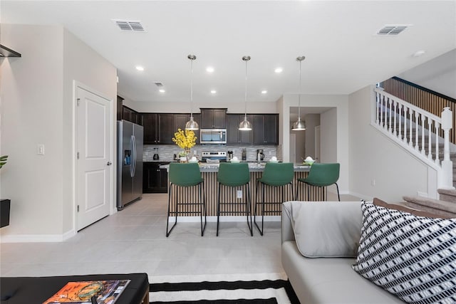 kitchen featuring dark brown cabinetry, stainless steel appliances, pendant lighting, a breakfast bar area, and decorative backsplash