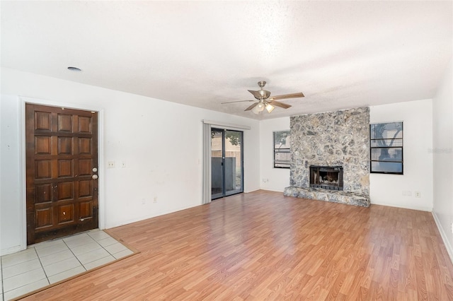 unfurnished living room with light wood-type flooring, a stone fireplace, and ceiling fan