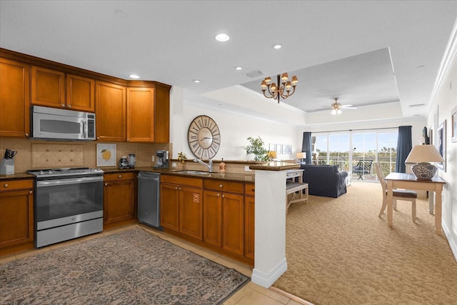 kitchen with a tray ceiling, kitchen peninsula, sink, and appliances with stainless steel finishes