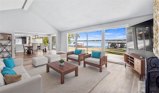 living room with a water view, lofted ceiling with beams, a textured ceiling, and light wood-type flooring