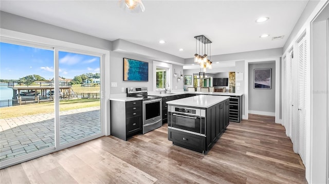 kitchen featuring sink, appliances with stainless steel finishes, decorative light fixtures, kitchen peninsula, and light wood-type flooring