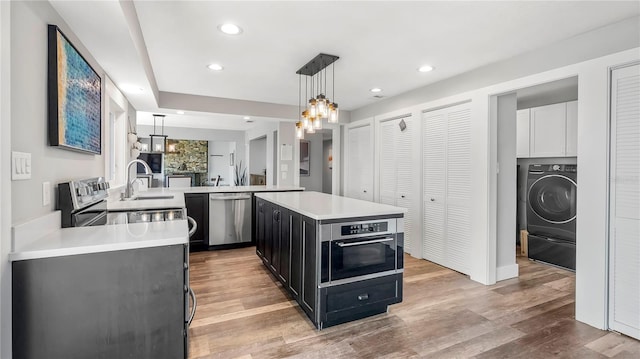 kitchen featuring a kitchen island, appliances with stainless steel finishes, washer / dryer, hanging light fixtures, and kitchen peninsula