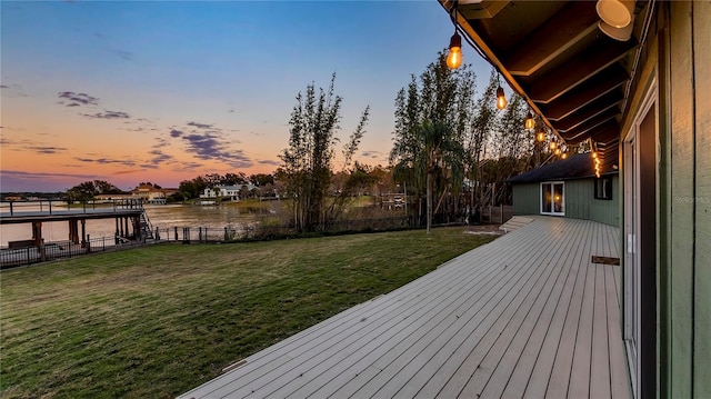 deck at dusk featuring a water view and a yard