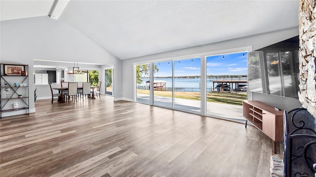 living room featuring an inviting chandelier, wood-type flooring, vaulted ceiling with beams, a water view, and a textured ceiling