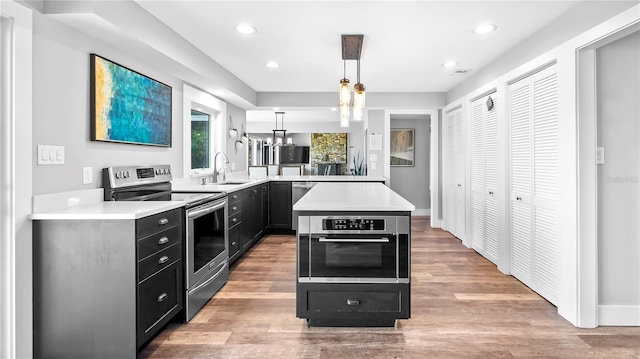 kitchen with sink, decorative light fixtures, light wood-type flooring, appliances with stainless steel finishes, and kitchen peninsula