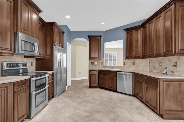 kitchen featuring decorative backsplash, light tile patterned floors, dark brown cabinetry, and stainless steel appliances