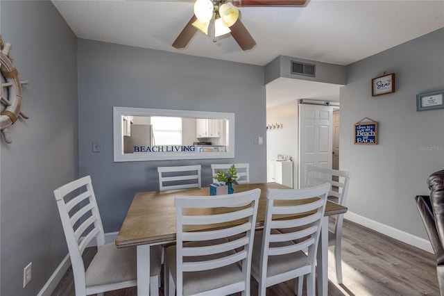 dining space featuring ceiling fan, a barn door, a textured ceiling, and light hardwood / wood-style flooring