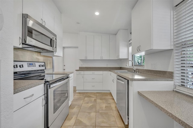 kitchen with appliances with stainless steel finishes, vaulted ceiling, sink, light tile patterned floors, and white cabinets