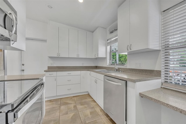 kitchen with appliances with stainless steel finishes, light tile patterned floors, white cabinetry, and sink