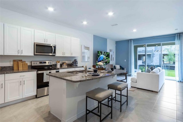 kitchen featuring a breakfast bar, stainless steel appliances, a kitchen island with sink, sink, and white cabinets