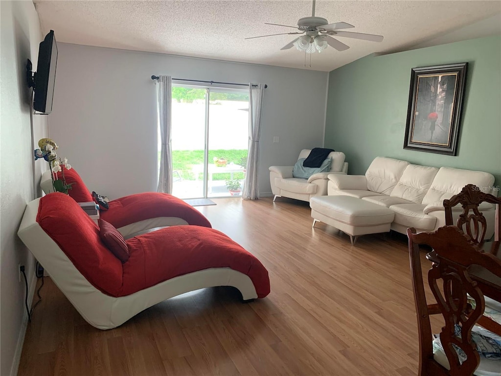 living room featuring ceiling fan, a textured ceiling, and light wood-type flooring