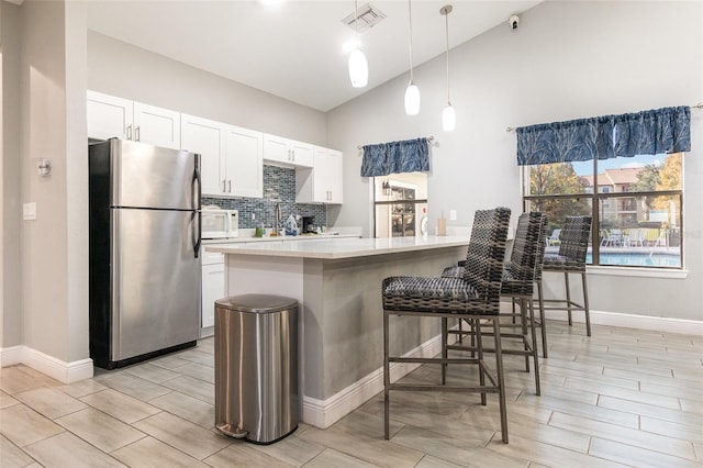 kitchen with white cabinets, light hardwood / wood-style flooring, decorative light fixtures, a kitchen bar, and stainless steel refrigerator