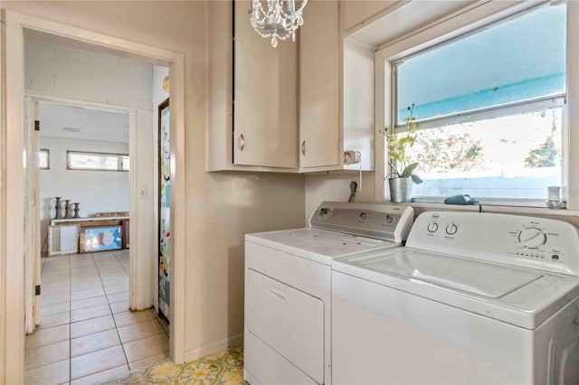 clothes washing area with washing machine and clothes dryer, a chandelier, light tile patterned floors, and cabinets