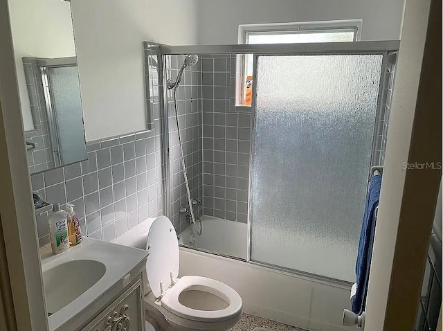 full bathroom with tasteful backsplash, combined bath / shower with glass door, toilet, vanity, and tile walls