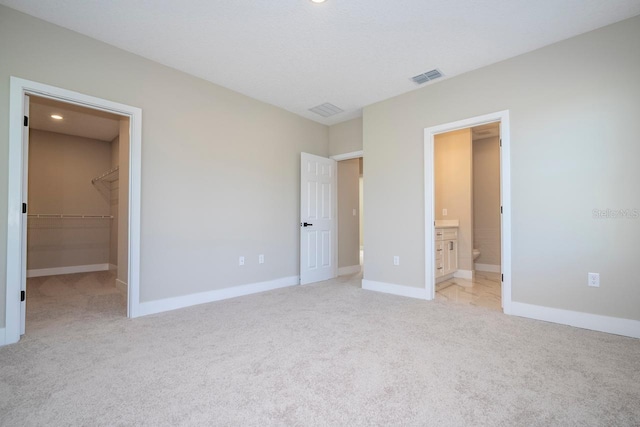 unfurnished bedroom featuring light carpet, ensuite bathroom, a spacious closet, and a closet