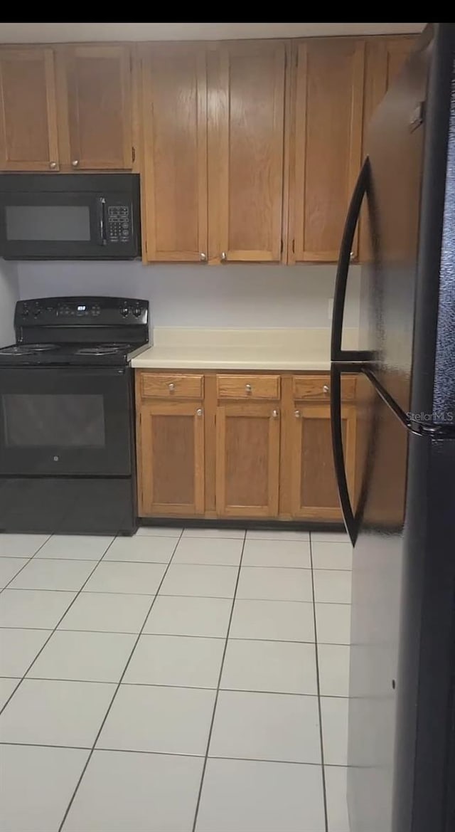 kitchen featuring black appliances, light tile patterned flooring, and light countertops