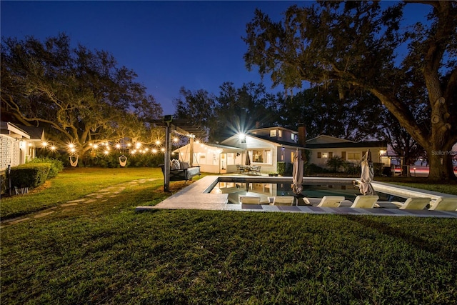 back house at twilight featuring a patio area and a lawn