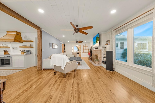 living room featuring ceiling fan, ornamental molding, light wood-type flooring, and a fireplace