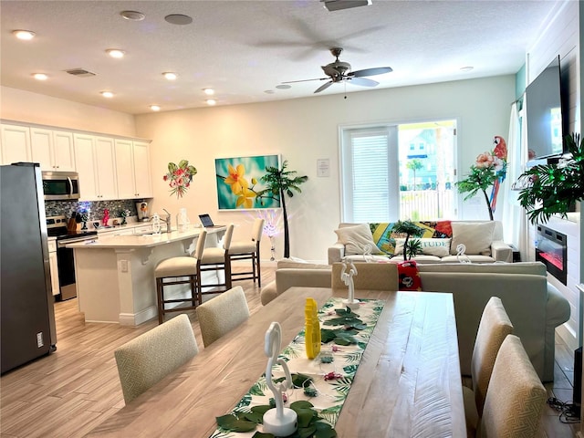 dining space featuring a textured ceiling, light wood-type flooring, ceiling fan, and sink