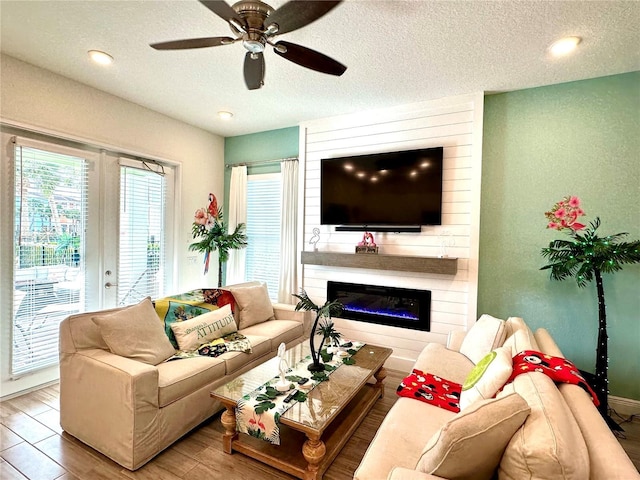 living room featuring ceiling fan, a fireplace, wood-type flooring, and a textured ceiling