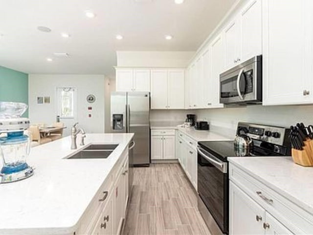 kitchen featuring white cabinetry, sink, an island with sink, appliances with stainless steel finishes, and light wood-type flooring