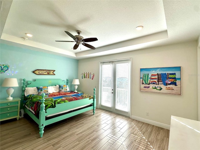 bedroom featuring french doors, access to outside, a raised ceiling, ceiling fan, and wood-type flooring