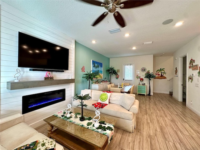 living room with a fireplace, ceiling fan, a textured ceiling, and light hardwood / wood-style flooring