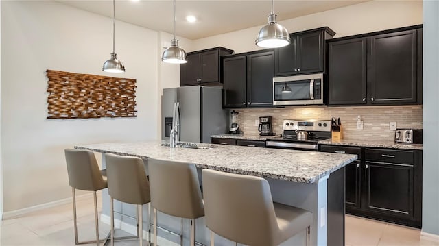 kitchen with decorative backsplash, a center island with sink, decorative light fixtures, and appliances with stainless steel finishes