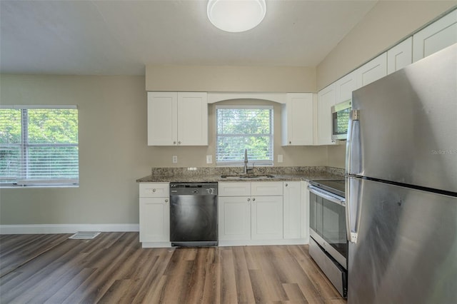 kitchen featuring stainless steel appliances, sink, dark stone countertops, white cabinets, and hardwood / wood-style floors