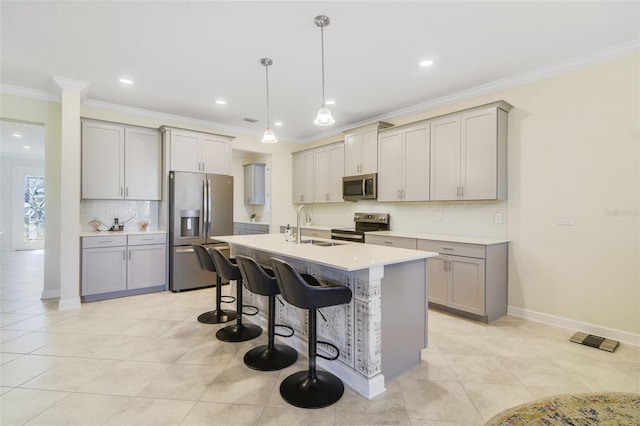 kitchen with gray cabinetry, sink, decorative light fixtures, a kitchen bar, and appliances with stainless steel finishes