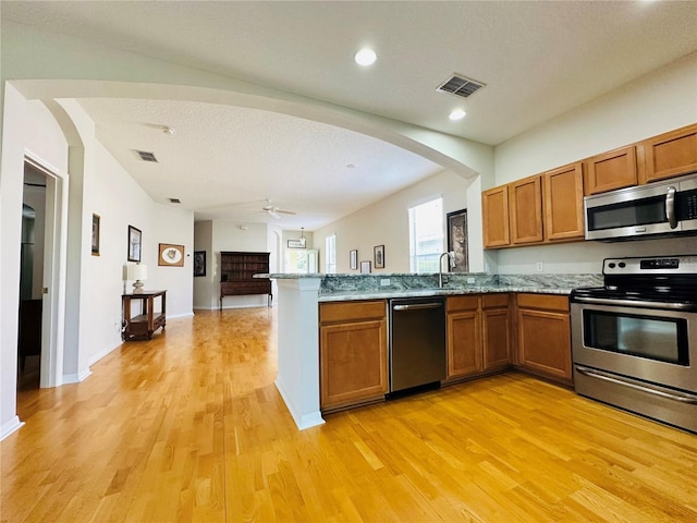 kitchen with kitchen peninsula, stainless steel appliances, a textured ceiling, and light wood-type flooring