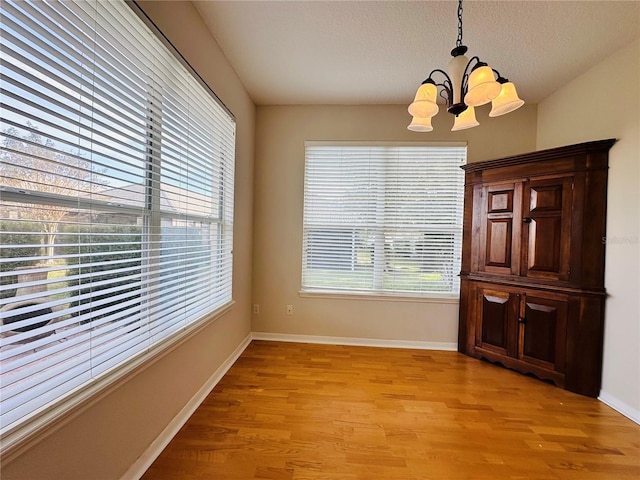 unfurnished dining area featuring vaulted ceiling, a chandelier, a textured ceiling, and light wood-type flooring