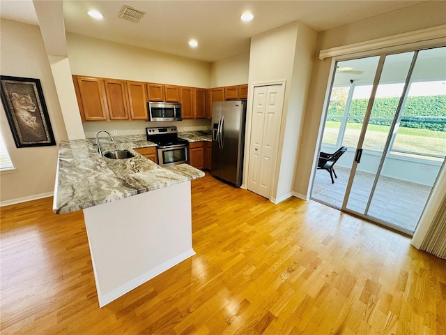 kitchen featuring sink, light stone counters, kitchen peninsula, appliances with stainless steel finishes, and light wood-type flooring