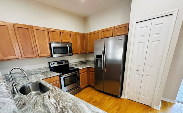 kitchen with light stone counters, sink, stainless steel appliances, and light hardwood / wood-style flooring