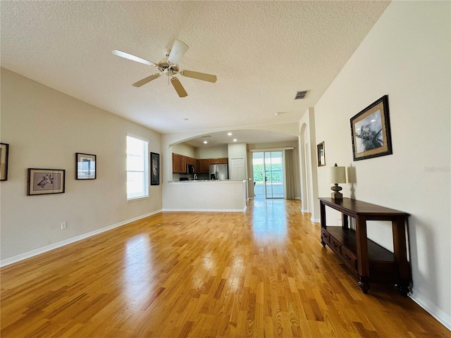 unfurnished living room featuring ceiling fan, a textured ceiling, and light hardwood / wood-style flooring