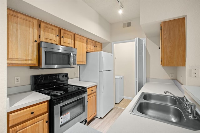 kitchen with washer and clothes dryer, rail lighting, sink, light hardwood / wood-style flooring, and stainless steel appliances